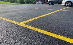 Freshly sealcoated parking lot with crisp yellow line striping, providing a smooth, protected asphalt surface for vehicles.