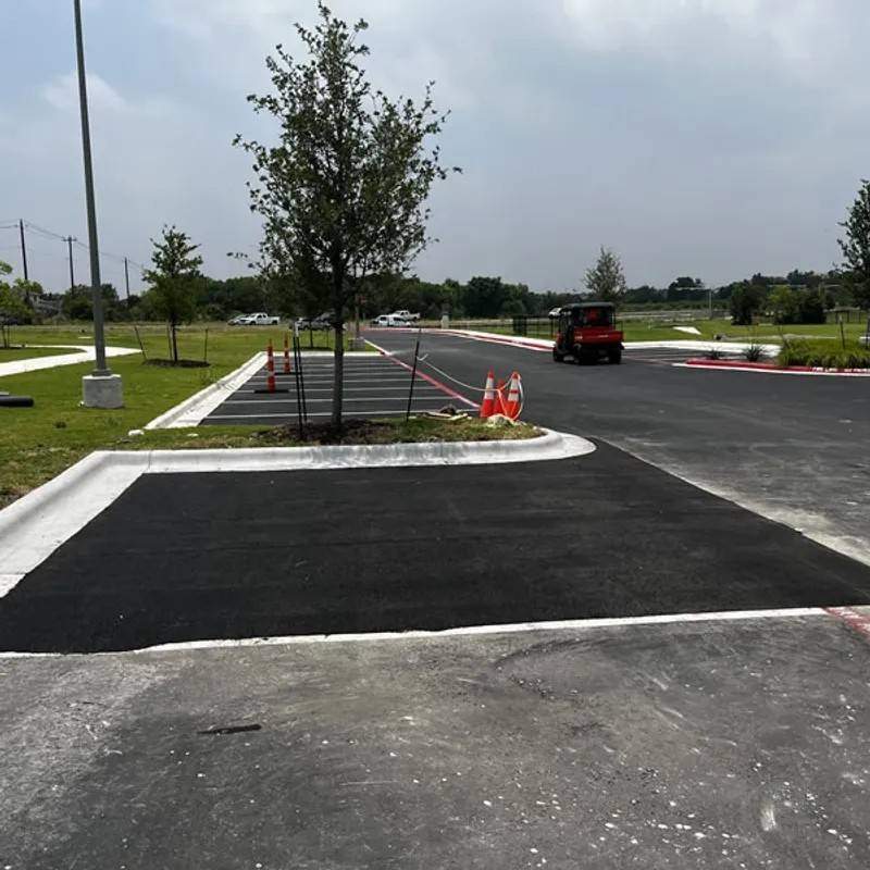 Freshly paved and sealed black asphalt parking lot with white concrete curbs, orange traffic cones, and landscaping trees, showcasing a commercial asphalt maintenance project by Black Rock Industries.