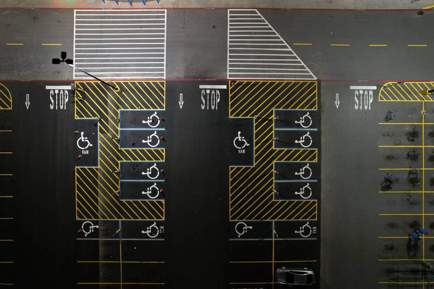 Directly overhead drone view of a freshly painted parking lot, showcasing newly striped yellow and white lines, a crosswalk, "STOP" stencils, and blue-outlined accessible parking spaces with handicap symbols by Black Rock Industries.
