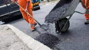 Paving crew shoveling hot asphalt along a concrete curb during ADA compliance sidewalk and ramp upgrades