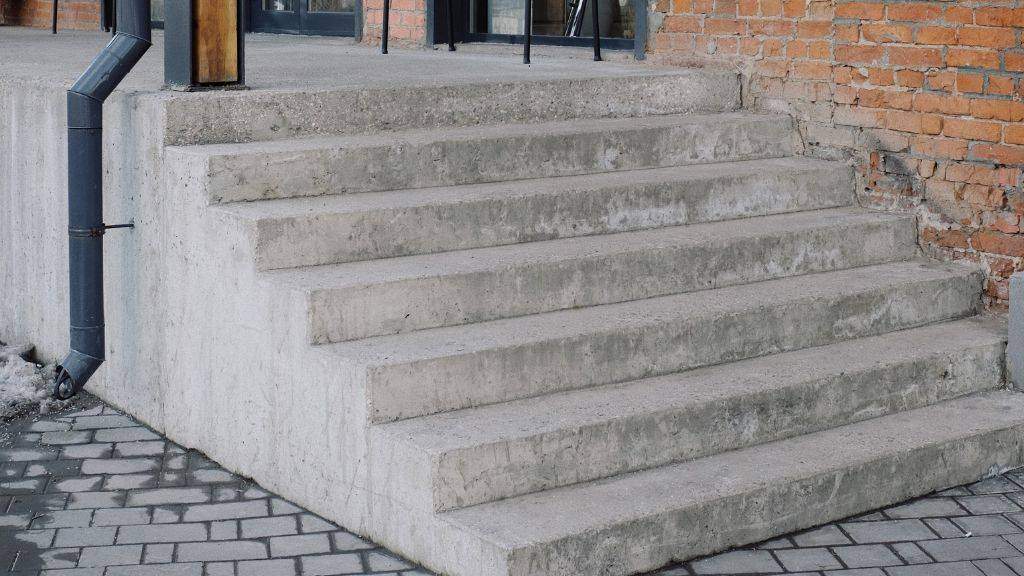Concrete outdoor entryway stairs requiring ADA handrail and ramp upgrades for commercial property accessibility.