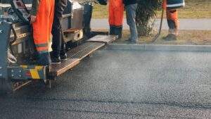 Paving crew operating heavy asphalt machinery during fall commercial pavement maintenance and resurfacing