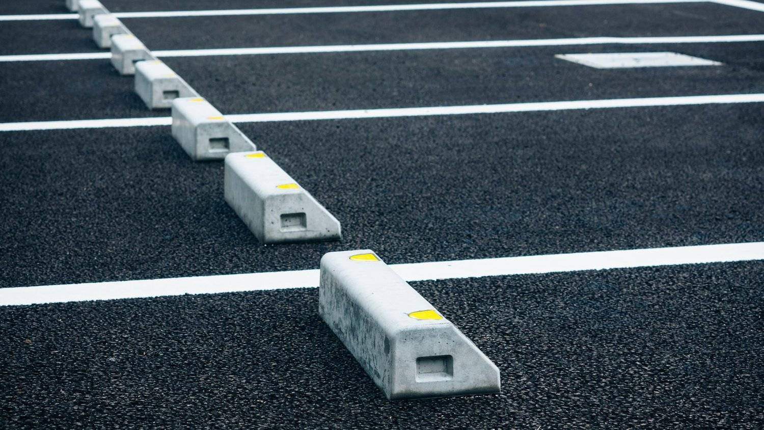 Clean commercial asphalt parking lot featuring concrete wheel stops and fresh white line striping