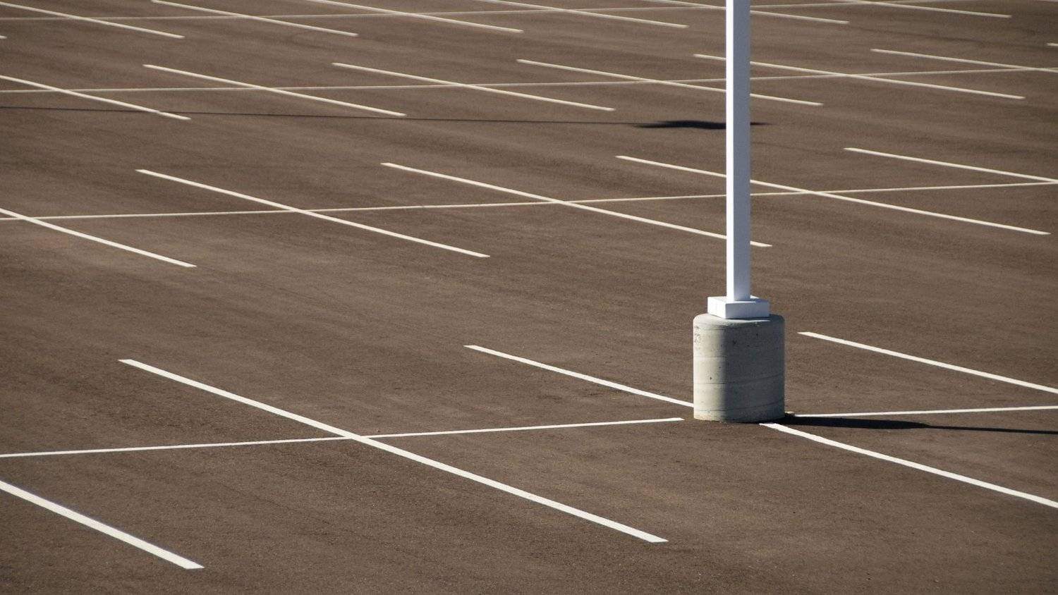Vast commercial parking lot with crisp line striping and light pole foundations prepared for heavy seasonal traffic and rain.
